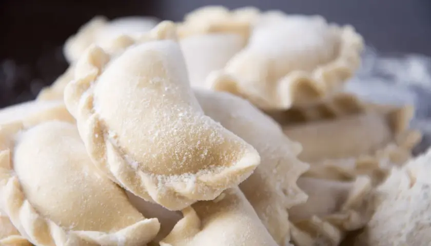 Zbliżenie na surowe, mrożone pierogi posypane mąką.