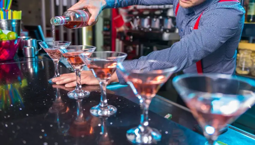 Barman nalewa różowy drink do kieliszków na barze.