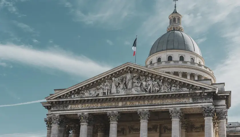 Majestatyczny Panteon w Paryżu z kopułą i francuską flagą na tle błękitnego nieba.