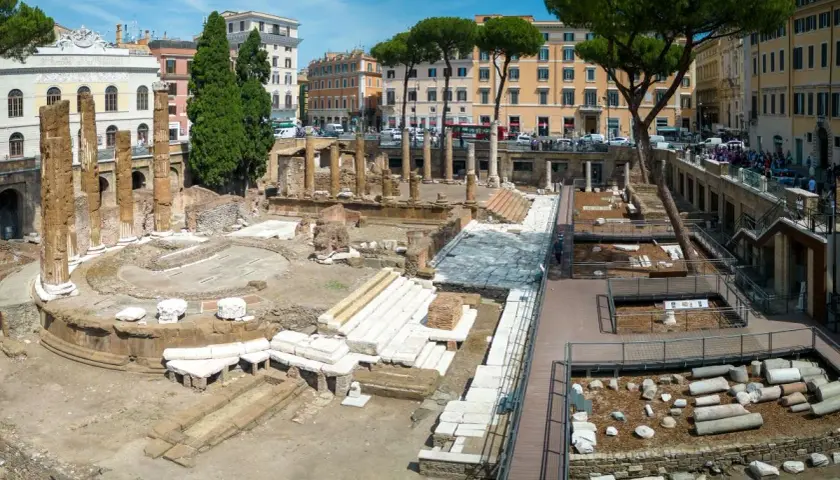 Antiche rovine dell'area sacra di Largo Argentina a Roma, con colonne e resti di templi sotto un cielo azzurro.