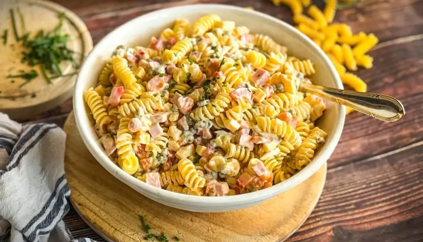 Herzhafter Nudelsalat mit Fleischsalat, Erbsen und einer cremigen Sauce, garniert mit frischen Kräutern.