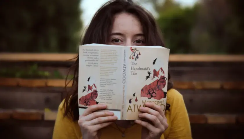 Dziewczyna w żółtej bluzce czyta książkę po angielsku "The Handmaid's Tale" Margaret Atwood.