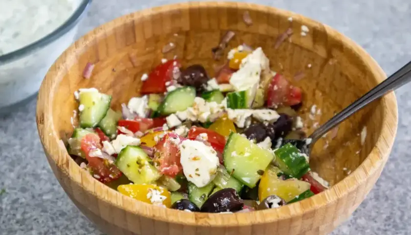En härlig grekisk sallad med tomater, gurka, oliver och fetaost i en träskål.