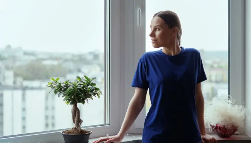 Kobieta wpatruje się w miasto przez okno, ciesząc się spokojem i pewnością, jaką daje gwarancja na okna.