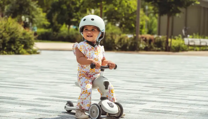 Uśmiechnięte dziecko w kasku na jeździku Scoot and Ride od kiedy zaczęło swoją przygodę z jazdą.