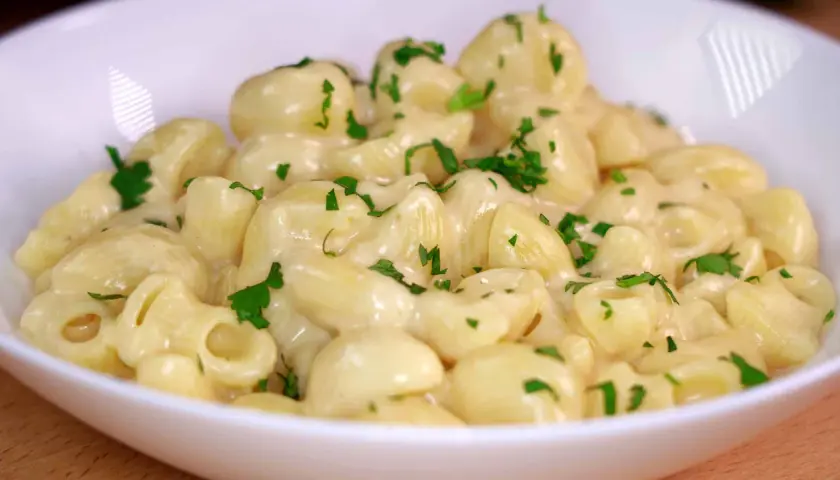 Mac and cheese cremoso, con trozos de perejil fresco espolvoreados. Un plato reconfortante y delicioso.
