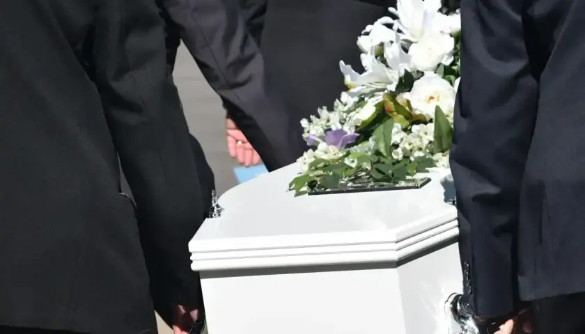 Biała trumna z kwiatami niesiona przez żałobników. Zastanawiasz się, ile kosztuje trumna?