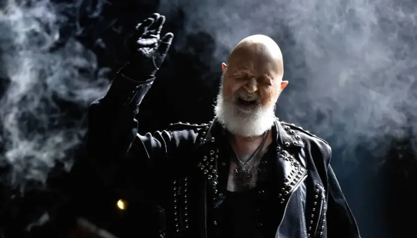 Rob Halford z Judas Priest, w skórzanej kurtce z ćwiekami, wznosi rękę w geście, jakby wykrzykując "Panic Attack" na koncercie.