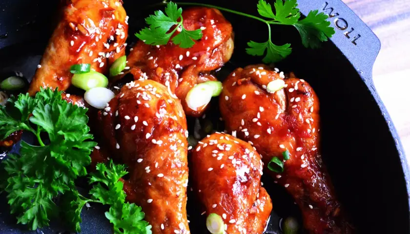 Kurczak teriyaki w glazurze z sezamem i szczypiorkiem w czarnej patelni.