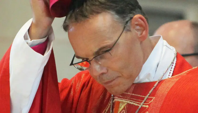 Bischof Tebartz van Elst trägt eine rote Messrobe und eine weiße Halskrause. Er blickt nach unten, während er eine Kopfbedeckung aufsetzt.