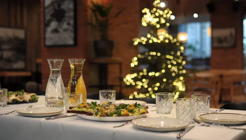 Stół wigilijny z przystawkami, napojami i ozdobioną choinką w tle. Zamówienia na wigilię w restauracji.
