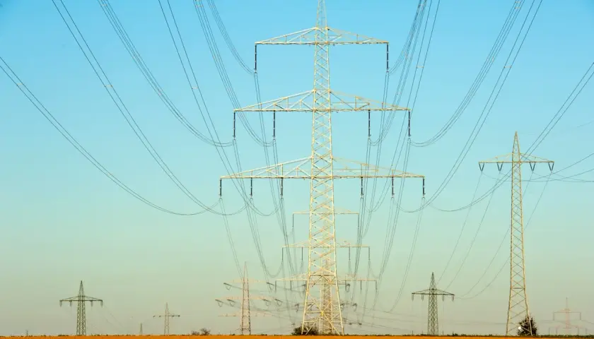 Linie energetyczne na tle błękitnego nieba. Wiele słupów wysokiego napięcia, tworzących sieć, jakby ilustrowało przelicznik MW na KW.