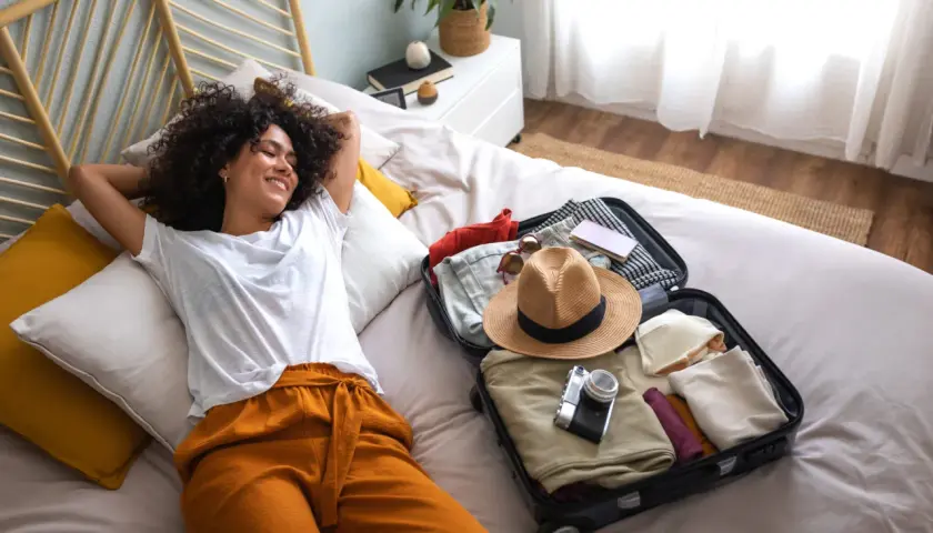 Une jeune femme se détend sur un lit, une valise ouverte à côté d'elle, prête pour son voyage. Elle est le parfait médiateur du tourisme, rêvant de nouvelles aventures.