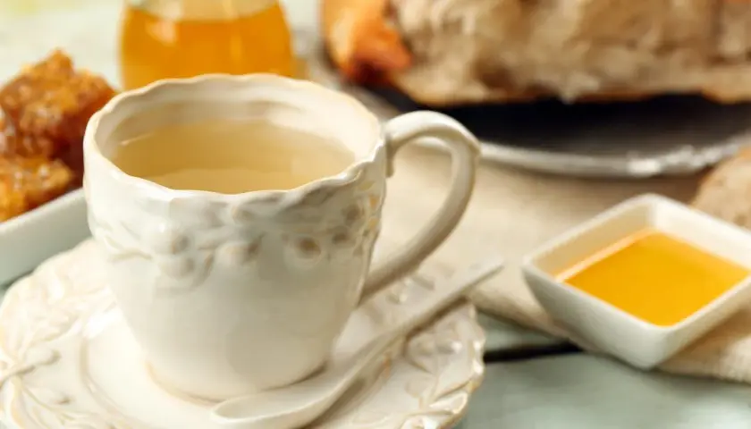 Ciepła herbatka imbirowa w ozdobnej filiżance, obok miód i kawałek chleba. Idealny poranek.