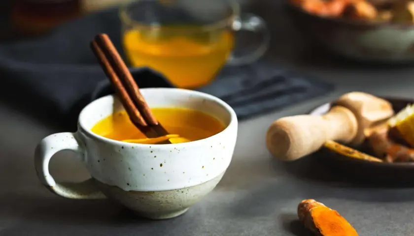 Eine Tasse goldener Ingwer-Kurkuma-Tee mit Zimtstange. Perfekt, um ihn abends zu trinken.