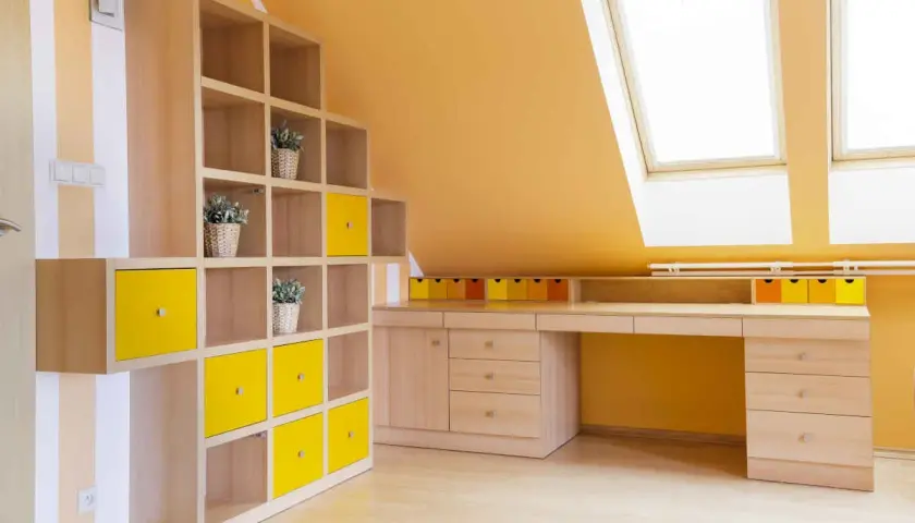 Colori vivaci per le pareti di una mansarda: arancione acceso e tocchi di giallo su una libreria modulare.