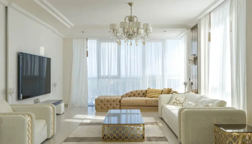 Elegancki salon w stylu nowojorskim, z jasnymi sofami, złotymi akcentami i kryształowym żyrandolem.