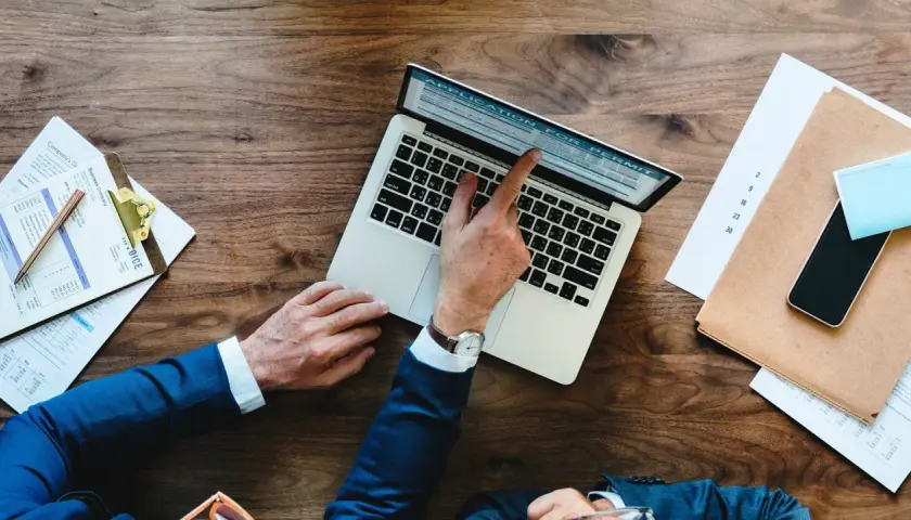 Biznesmen wypełnia wniosek o pozwolenie (application for permit) na laptopie. Obok leżą dokumenty i telefon.