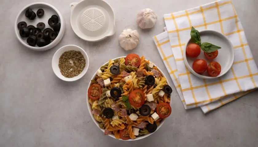 Deliciosa ensalada de pasta italiana con tomates, aceitunas, queso y salami. Ingredientes frescos listos para servir.