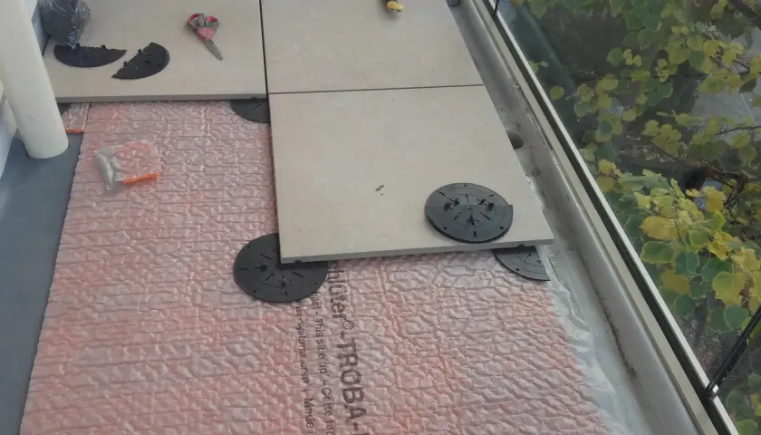 Installazione di un pavimento galleggiante su guaina bituminosa, con piastrelle in fase di posa su supporti regolabili.