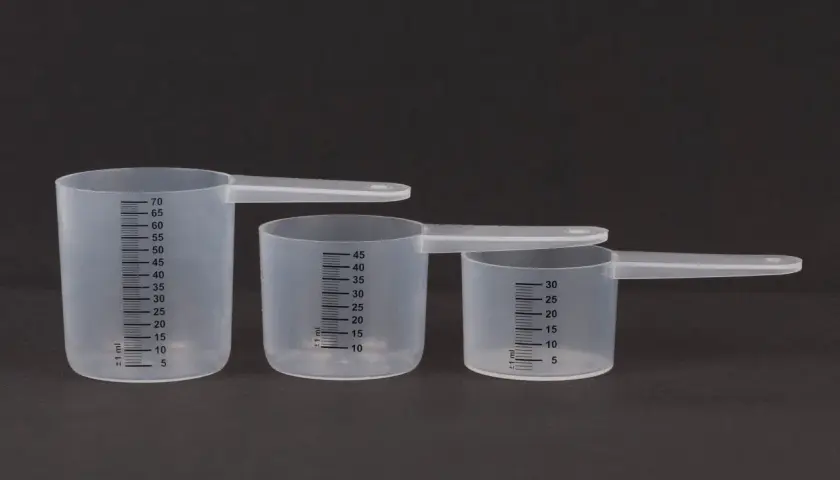 Trzy plastikowe miarki kuchenne z podziałką w mililitrach na ciemnym tle.