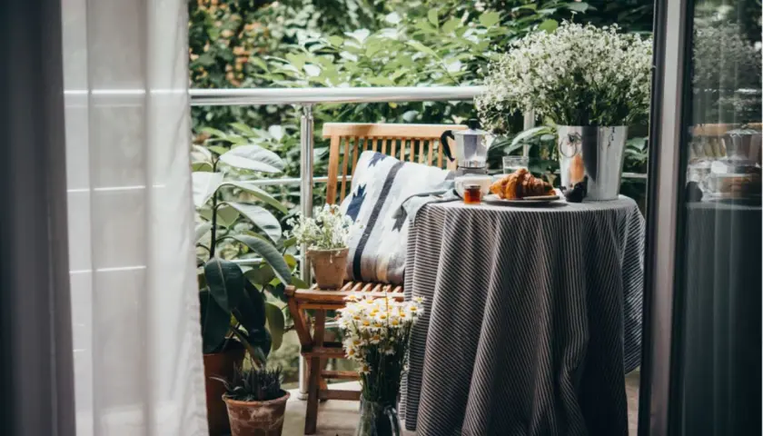 Gemütlich einen kleinen Balkon einrichten: Frühstück mit Croissant und Kaffee auf dem Tisch, umgeben von Pflanzen.