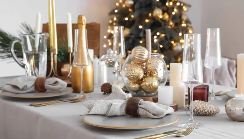 Festlich gedeckter Tisch Weihnachten mit goldenen Kugeln, Kerzen und Champagner. Ein eleganter Blickfang für die Feiertage.
