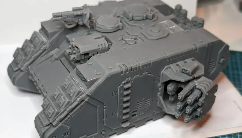 Szary model Land Raider Redeemer, gotowy do malowania, z działkiem na dachu i wyrzutniami flamerów po bokach.