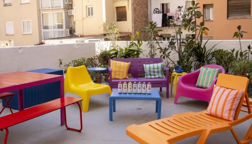 Un colorido conjunto de muebles de terraza, listo para pintar. Sillas, bancos y mesas en vibrantes tonos, con latas de spray dispuestas para dar vida a este espacio exterior.