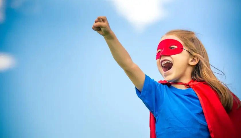 Ein Kind im Superhelden-Kostüm mit rotem Cape und Maske, bereit für den ablauf einschulung.