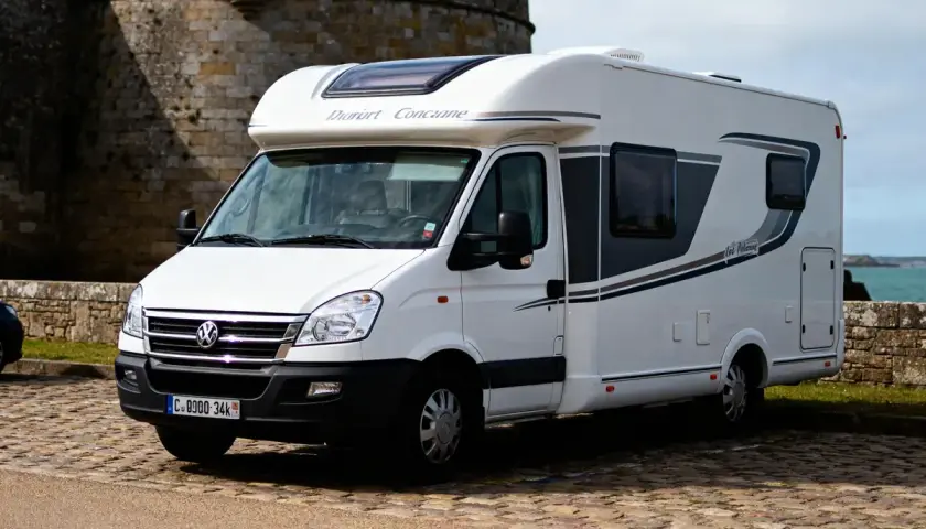 Un camping-car blanc "Dauphin Concarneau" stationné sur un sol pavé, avec un mur de pierre et la mer en arrière-plan. Un spot camping car Bretagne idéal pour explorer la côte.
