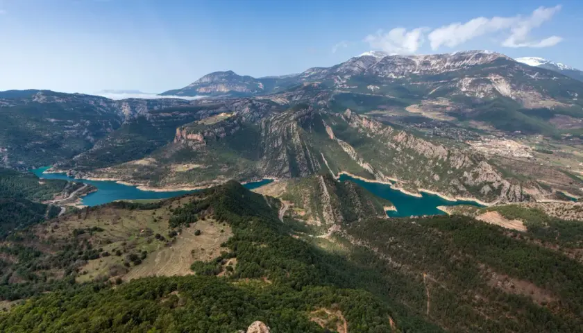 Paisaje montañoso con embalses de agua turquesa, ideal para explorar rutas Pirineos. Bosques verdes cubren las laderas y picos nevados al fondo.