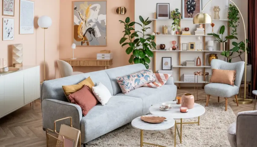 Soggiorno accogliente con divano grigio, cuscini decorativi e tavolini in marmo. Le pareti color pesca e gli arredi creano un'atmosfera rilassante, mostrando come i **colori pastello quali sono** perfetti per un ambiente sereno.