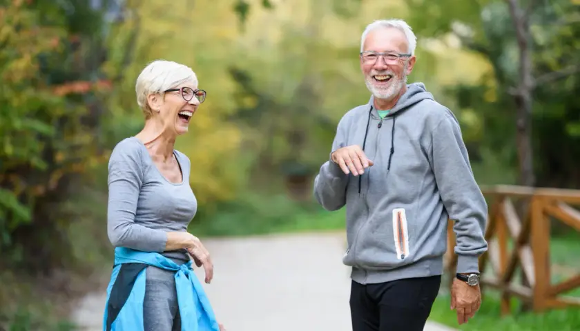 Ein lachendes älteres Paar genießt einen Spaziergang im Park. Bewegung hält sie geistig fit und glücklich.