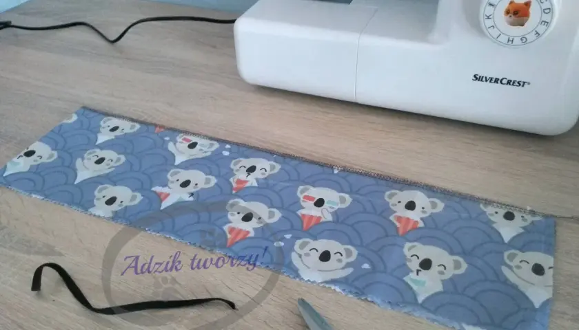 Materiały do szycia gumki do włosów: tkanina z misiami koala, czarna gumka i maszyna do szycia.