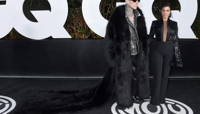 Travis Barker i jego żona Kourtney Kardashian na ściance GQ. Travis w ekstrawaganckim futrze, Kourtney w eleganckim garniturze.