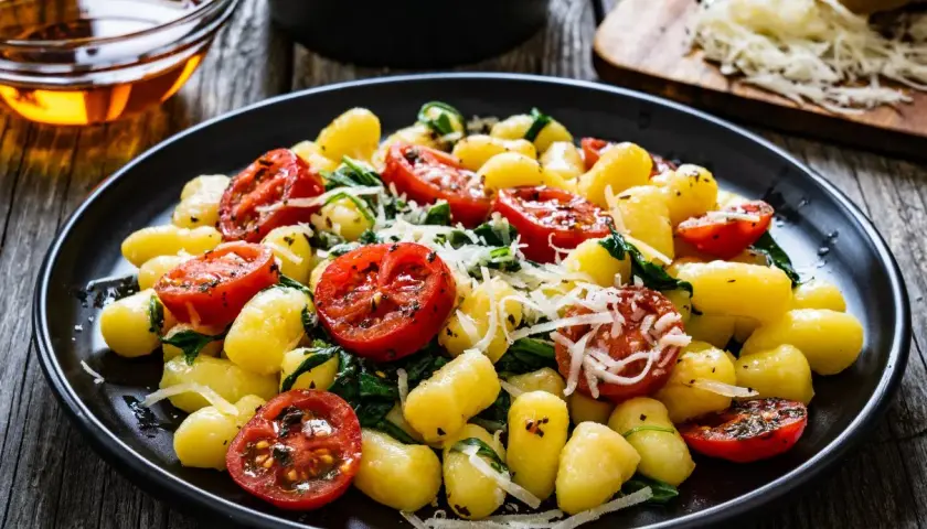 Pyszne gnocchi szpinakowe z pomidorkami koktajlowymi i parmezanem na drewnianym stole.