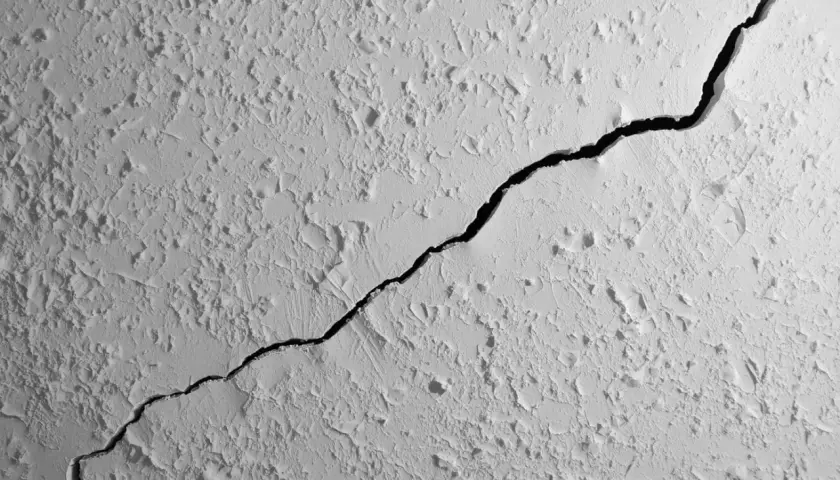 Une fissure traverse le plafond texturé d'un appartement, révélant une ombre profonde.