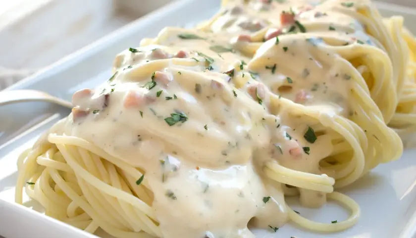 Spaghetti mit cremiger Carbonara-Sauce und Speckstücken, garniert mit Petersilie.