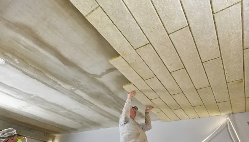 Pracownicy montują płyty izolacyjne, wykonując ocieplenie stropu betonowego.
