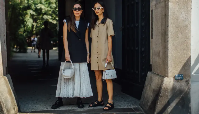 Deux femmes stylées montrent comment porter blazer sans manche femme. L'une porte un blazer noir sur une jupe plissée, l'autre une robe chemise beige.