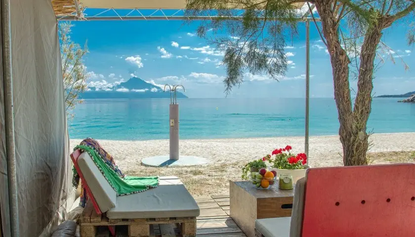 Relaks przy plaży w Armenistis Camping. Leżaki, stolik z owocami i widok na morze z górą w oddali.