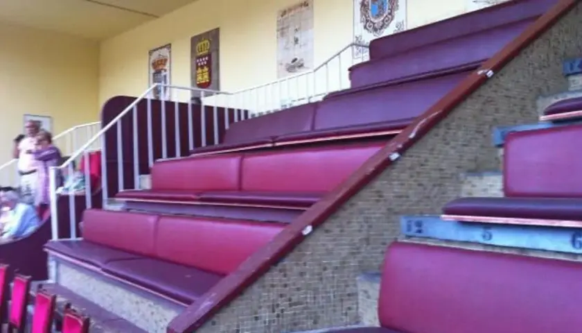 Asientos de terciopelo rojo en un palco de las ventas, con escaleras y barandillas blancas.