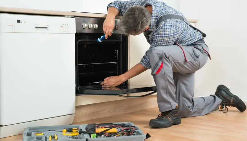 Un technicien effectue le branchement d'un four encastrable, outils à portée de main.