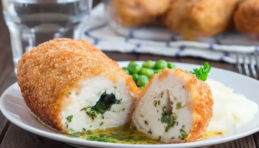 Pyszny kotlet po kijowsku, chrupiący z zewnątrz, soczysty w środku, z zielonym nadzieniem. Podany z puree i groszkiem.
