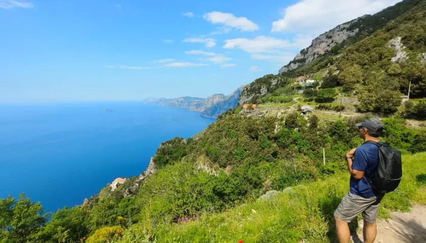 Hiker on a cliff path overlooking the blue sea and coastline.