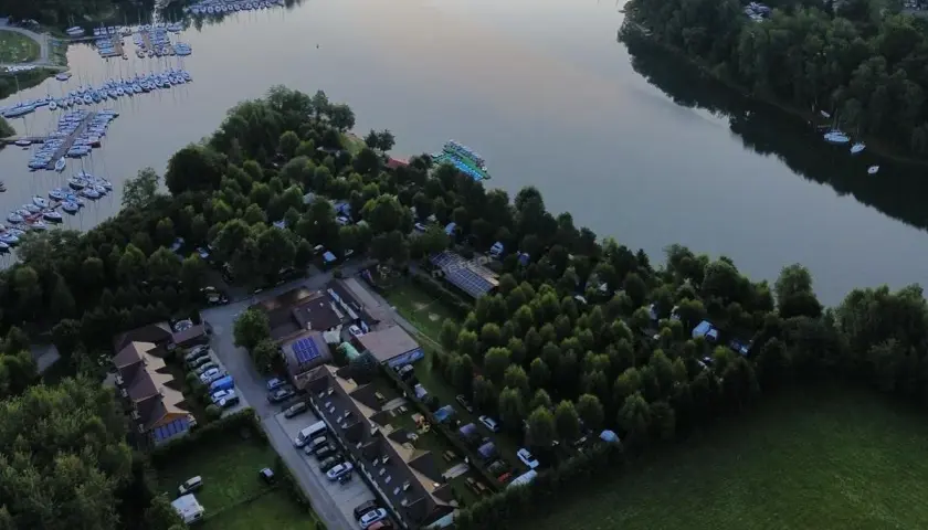 Malowniczy widok na camping w Polańczyku nad jeziorem, z łodziami na wodzie i zielonymi drzewami.