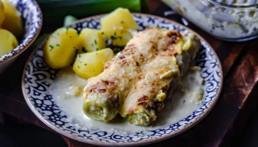 Gebackener Lauch mit Schinken, überbacken mit Käse, serviert mit Salzkartoffeln und einer cremigen Sauce.