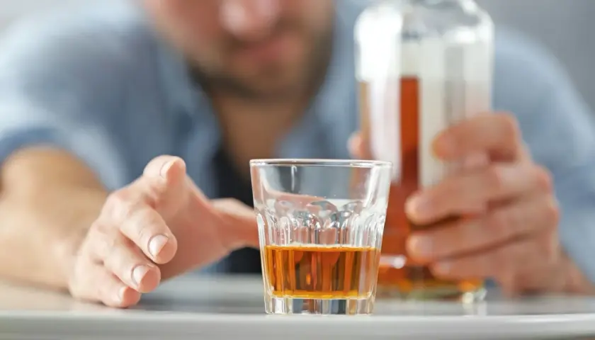 Mężczyzna sięga po szklankę z alkoholem, grozi mu zatrucie alkoholowe.