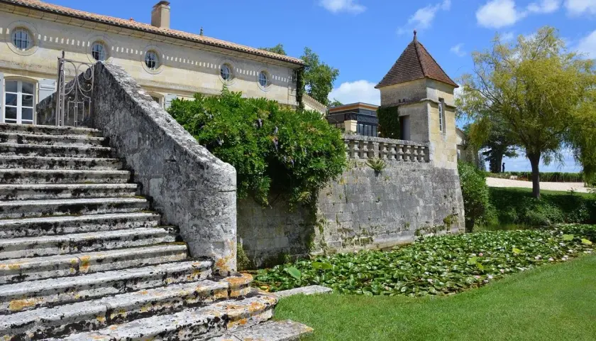 Escalier de pierre menant à un château, avec un étang de nénuphars. Une belle journée pour une visite château Pomerol.
